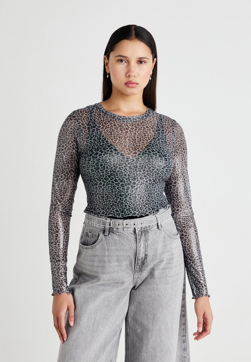 Sheer long-sleeve top featuring a grey and black leopard print, scoop neckline, and scalloped hem, paired with high-waisted grey jeans.