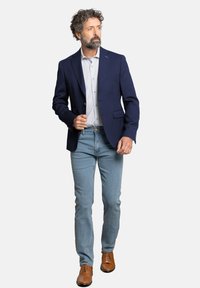 Blazer navy, camisa blanca con patrón, jeans azul claro, zapatos marrones. El blazer tiene dos bolsillos frontales y un cierre de botón único. Corte ajustado.