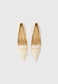 Beige pointed-toe pumps with a smooth leather finish, featuring a gold-tone chain accent across the front and a slender heel.