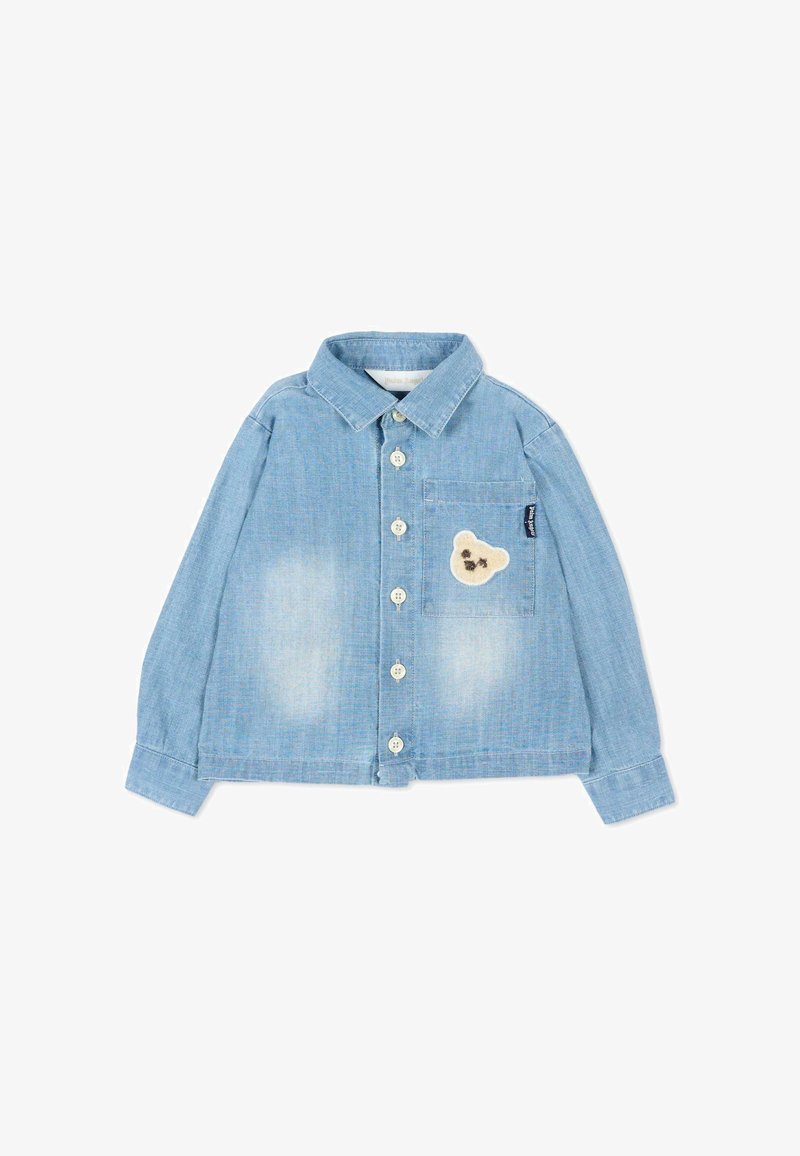 Chemise en denim bleu clair à boutons, manches longues, avec une poche poitrine ornée d'un petit écusson en forme de tête d'ours beige.