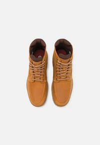 Botas altas de couro castanho com atacadores beges, com colarinho acolchoado e bico arredondado. Superfície texturizada e forro interior castanho em contraste.