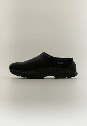 Sort slip-on sko med tyk tekstureret sål og lav hælkappe, minimalistisk design og lille Calvin Klein logo på siden.