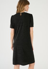 Abito nero con maniche a palloncino corte, caratterizzato da un tessuto texturizzato con una sottile lucentezza, e un collo rotondo con dettaglio a chiave sul retro.