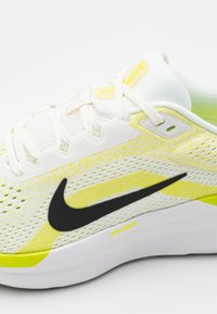 Chaussure de sport blanche et jaune néon avec dessus en maille, logo swoosh noir et semelle blanche. Comprend des lacets et des accents de soutien.