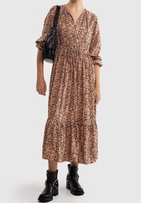 Robe midi imprimée léopard en tissu léger avec un décolleté en V et des manches bouffantes, associée à des bottines noires et un petit sac noir.