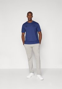 Marineblaue Baumwoll-T-Shirt mit dem "Champion"-Logo in Tinte, kombiniert mit hellgrauen Jogginghosen und weißen Turnschuhen.