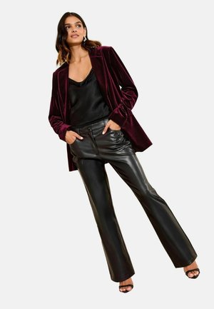 Samtiger burgunderfarbener Blazer über einem schwarzen Satin-Camisole und schwarzen Lederhosen. Das Outfit zeichnet sich durch elegante Linien und hohe Sandalen aus.