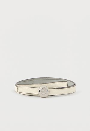 Cinturón de cuero crema con una hebilla plateada redonda que presenta un logo en relieve, exhibido enrollado sobre un fondo blanco.