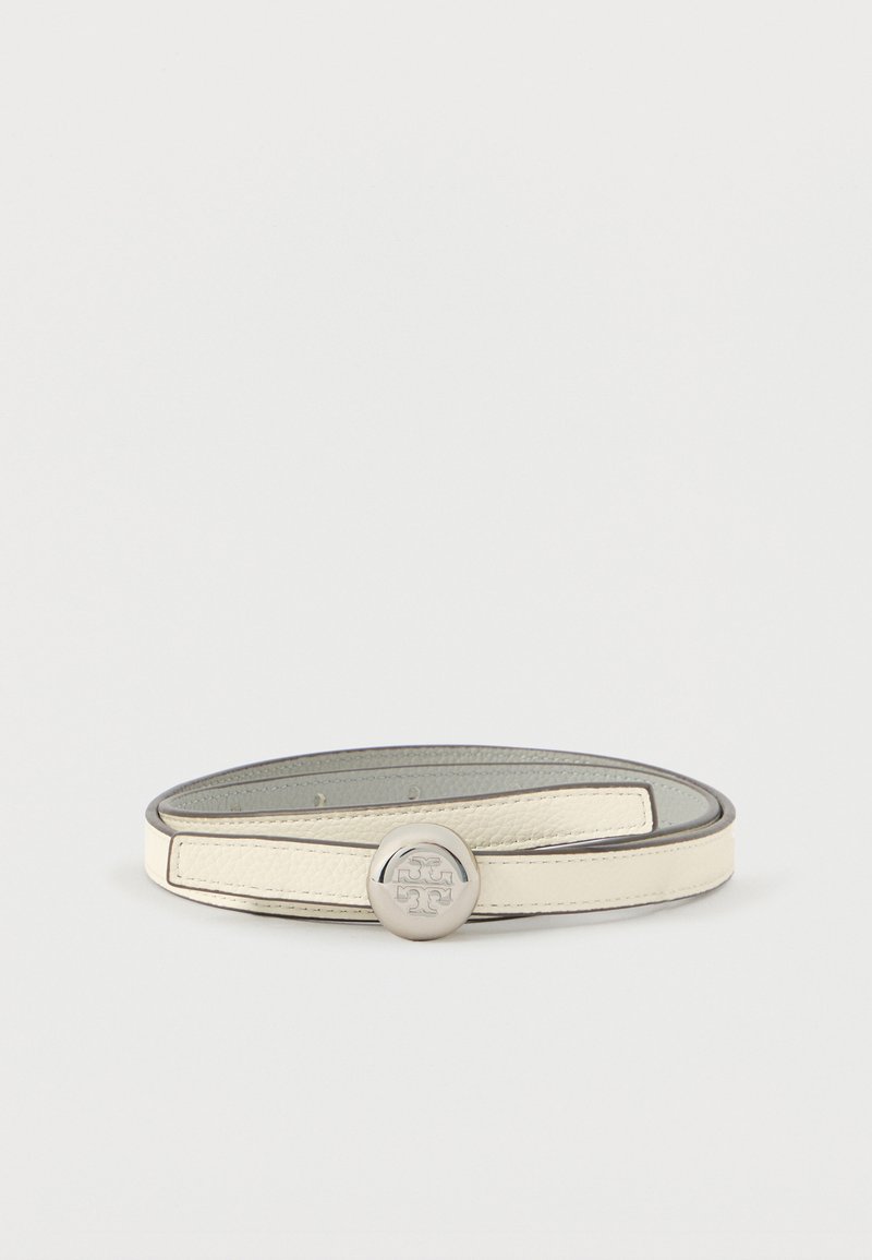 Kermanvärinen nahkavyö, jossa on pyöreä hopeanhohtoinen solki, jossa on kohokuvioitu logo, esillä valkoisella taustalla kierrettynä.