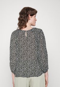 Blusa preta com estampado floral, mangas longas e bufantes, apresentando um detalhe de abertura nas costas e um tecido leve e transparente com padrões florais em branco e roxo.