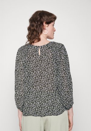 Blusa preta com estampado floral, mangas longas e bufantes, apresentando um detalhe de abertura nas costas e um tecido leve e transparente com padrões florais em branco e roxo.