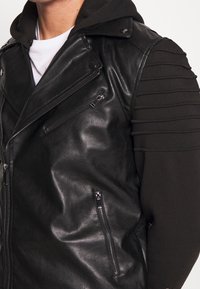 Giacca biker nera in pelle con zip frontale e due tasche laterali; presenta tessuto a costine sulle maniche con dettagli testurizzati.