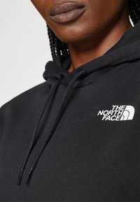 Black hoodie with a drawstring hood. Features The North Face logo in white on the left chest area. Smooth texture and casual fit.