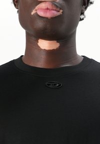Chemise noire à manches courtes avec un col rond et un petit logo brodé. Le tissu semble lisse et extensible.