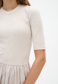 Helles beige, geripptes Oberteil mit kurzen Ärmeln, das in einen sanften, beigen, plissierten Rock übergeht. Glatte Textur, lässiges Design mit lockerer Passform.