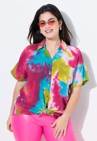 La maglietta a maniche corte tie-dye presenta colori vivaci di rosa, blu, verde e giallo, con una tasca singola e un design con orlo annodato.