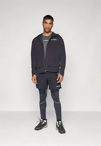 Sweat à capuche noir zippé avec logo, t-shirt athlétique gris, shorts noirs, leggings à motifs et baskets noires. Présente une coupe slim et un tissu lisse.