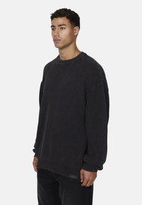 Maglione a costine grigio scuro con scollatura rotonda e vestibilità over. Presenta spalle cadute e un tessuto strutturato. Piccola etichetta in fondo.