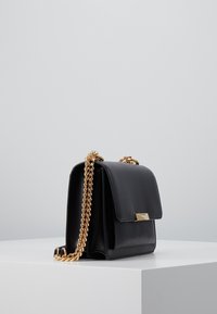 Černá kožená kabelka se zlatým řetízkovým popruhem, obdélníkového tvaru, s klopou na přední straně a lesklými zlatými kovovými doplňky.