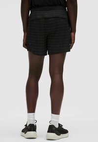 Mustat ruudulliset shortsit, jotka on valmistettu kevyestä kankaasta ja joissa on pehmeä vyötärö. Yhdistetty mustiin lenkkareihin ja valkoisiin nilkkasukkiin.