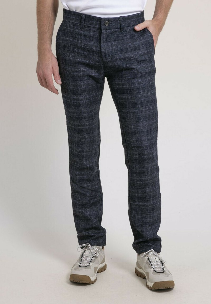 Pantalons à carreaux navy en tissu tissé, avec une coupe droite, des poches latérales et une fermeture à bouton. Associés à des chaussures de couleur claire.