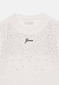Weißes Rundhals-Shirt mit schwarzem, zentriertem "Guess"-Logo, verziert mit verstreuten kleinen silbernen Strasssteinen auf der oberen Vorderseite.