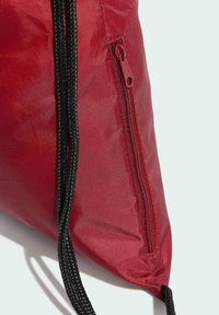 Sac en nylon rouge avec un cordon noir et une surface texturée, doté d'une poche zippée rouge. Forme compacte et triangulaire.