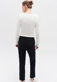 Vit långärmad topp med ribbat mönster, i kombination med svarta raka byxor. Outfiten kompletteras av vita sneakers.