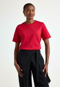 Rød bomulds T-shirt med korte ærmer og rund halsudskæring, parret med sorte bukser med bånd i taljen. Glat tekstur, afslappet design.