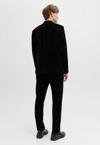 Melns samta uzvalks ar pielāgotu žaketi un atbilstošām biksēm. Iezīmējas ar gludu tekstūru un vienkāršu dizainu. Nēsāts ar melnām kurpēm.