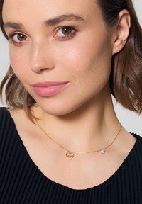 Złoty naszyjnik z łańcuszkiem z sercowym wisiorkiem z napisem "Mamma", akcentowany małą białą perłą. Gładka tekstura, delikatne ogniwa.