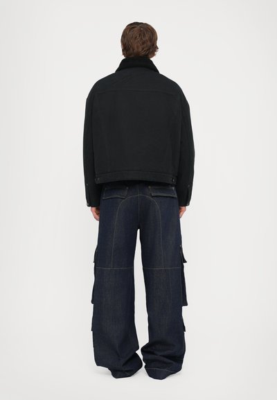 Black denim jacket with a shearling collar and long sleeves. Paired with baggy blue denim cargo pants featuring multiple pockets and contrasting stitching.