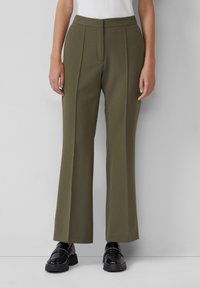 Pantaloni verde oliva a vita alta con gamba larga e pieghe frontali. Tessuto liscio con una vestibilità strutturata. Abbinati a mocassini neri in vernice.