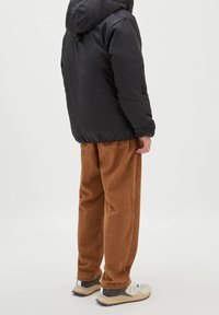 Doudoune noire avec capuche, pantalon en velours côtelé marron et baskets. La doudoune présente une texture lisse ; le pantalon a un motif côtelé.