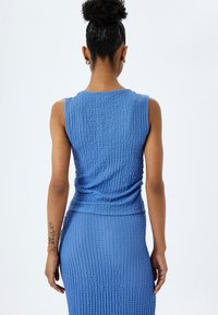 Top sin mangas azul hecho de una tela texturizada, con un diseño ajustado y detalle fruncido en la cintura, combinado con una falda a juego.
