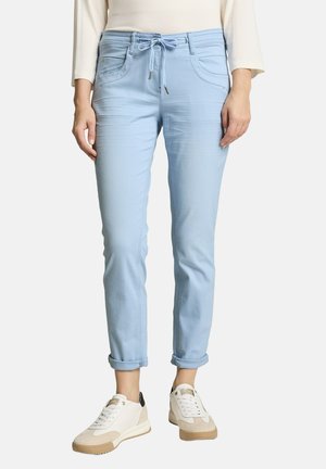 Hellblaue Slim-Fit-Hose mit Kordelzug in der Taille, hochgekrempelte Säume, kombiniert mit beigen und weißen Sneakern und einem leichten Langarmshirt.