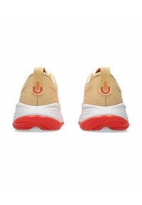 Baskets de sport jaunes et rouges avec un talon rembourré, une tige texturée et une semelle intermédiaire blanche. Comprend une sangle de traction et des détails de marque subtils.