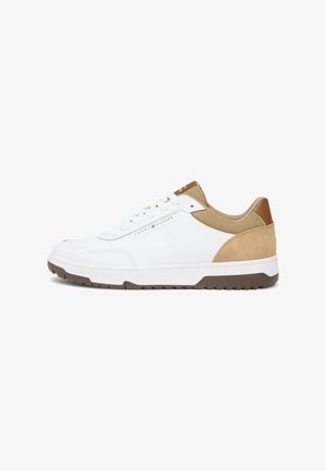 Zapatilla deportiva baja blanca con detalles en ante y malla color beige, suela de goma marrón y logo de "Tommy Hilfiger" en el lateral y la lengüeta.