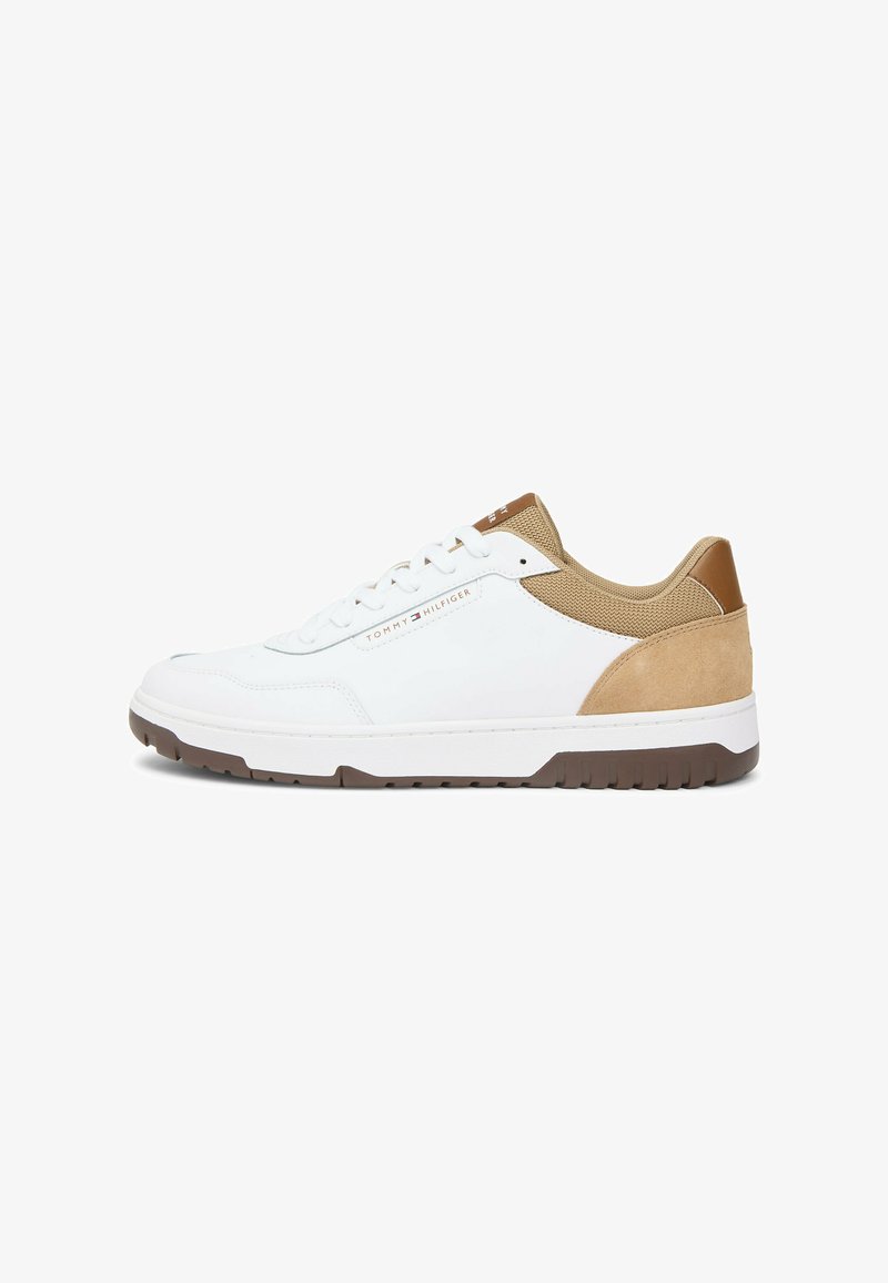 Witte lage sneaker met beige suède en mesh accenten, bruine rubberen zool, en "Tommy Hilfiger" logo op de zijkant en tong.