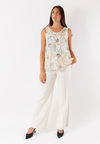 Top senza maniche floreale in tessuto leggero con fiori dai colori pastello. Abbinato a pantaloni ampi color crema e décolleté nere a punta.