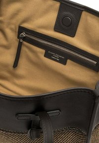 Zwarte leren handtas interieur met een tan kleurige stofvoering, met een ritszak en een label. Gladde textuur, minimalistisch ontwerp.