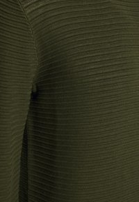 Gros plan d'un tissu tricoté côtelé vert foncé avec une couture visible le long d'une jonction, mettant en valeur la texture et le motif.