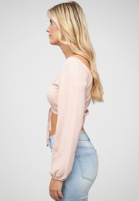 Cropped top rosa chiaro con maniche lunghe a sbuffo, tessuto texturizzato e lacci laterali, abbinato a jeans azzurri a vita alta.