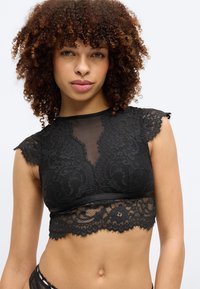 Μαύρο κορυφαίο τοπ από δαντέλα με διαφανείς πλαισιώσεις από τούλι, λουλουδένια μοτίβα και κυματιστές άκρες. Μαλακό ύφασμα με εφαρμοστή σιλουέτα και λεπτομερή σχεδιασμό.