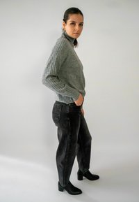 Grijze geribbelde gebreide trui met een hoge kraag, gecombineerd met hoge zwarte jeans en zwarte enkellaarsjes. Eenvoudig, gestructureerd ontwerp.