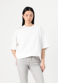 T-shirt blanc surdimensionné avec des manches courtes et un col rond, associé à un jean gris clair. Texture lisse, design minimaliste.