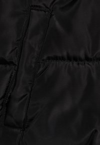 Czarny materiał kurtki puchowej o gładkiej, błyszczącej fakturze. Posiada poziome pikowane sekcje i ukrytą kieszeń.