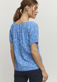 Blusa blu a fiori con maniche a sbuffo corte, scollo elastico, tessuto leggero e motivo floreale bianco sparso. Design semplice e con vestibilità ampia.