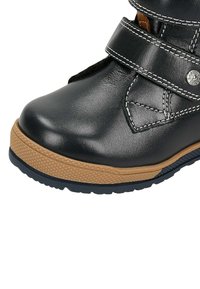 Stivaletto in pelle nera con doppia cucitura bianca, suola in gomma testurizzata color sabbia e una fascia nera con chiusura a scatto in metallo.