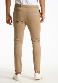 Chino kaki avec une coupe ajustée, présentant un devant plat, des poches latérales discrètes, deux poches arrière et des poignets retroussés.